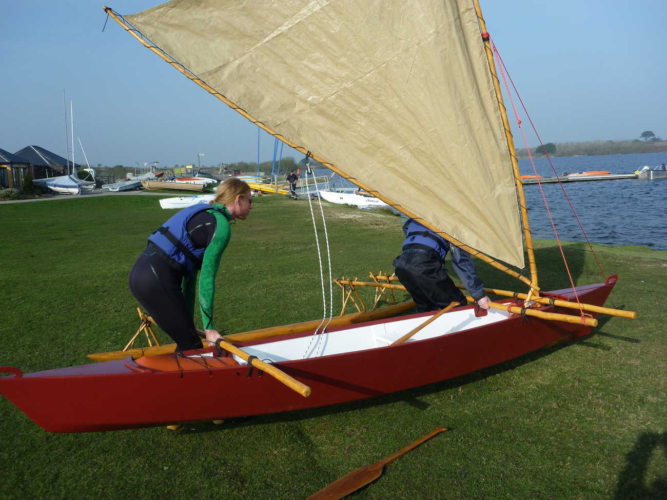 Red Melanesia outrigger canoe with crabclaw sail being carried by two towards the water