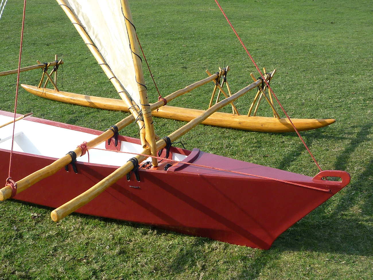 Dark red Melanesia outrigger canoe on land, close up of bow and float