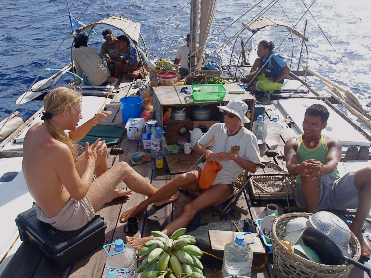 People talking and cooking on the deck of a double canoe