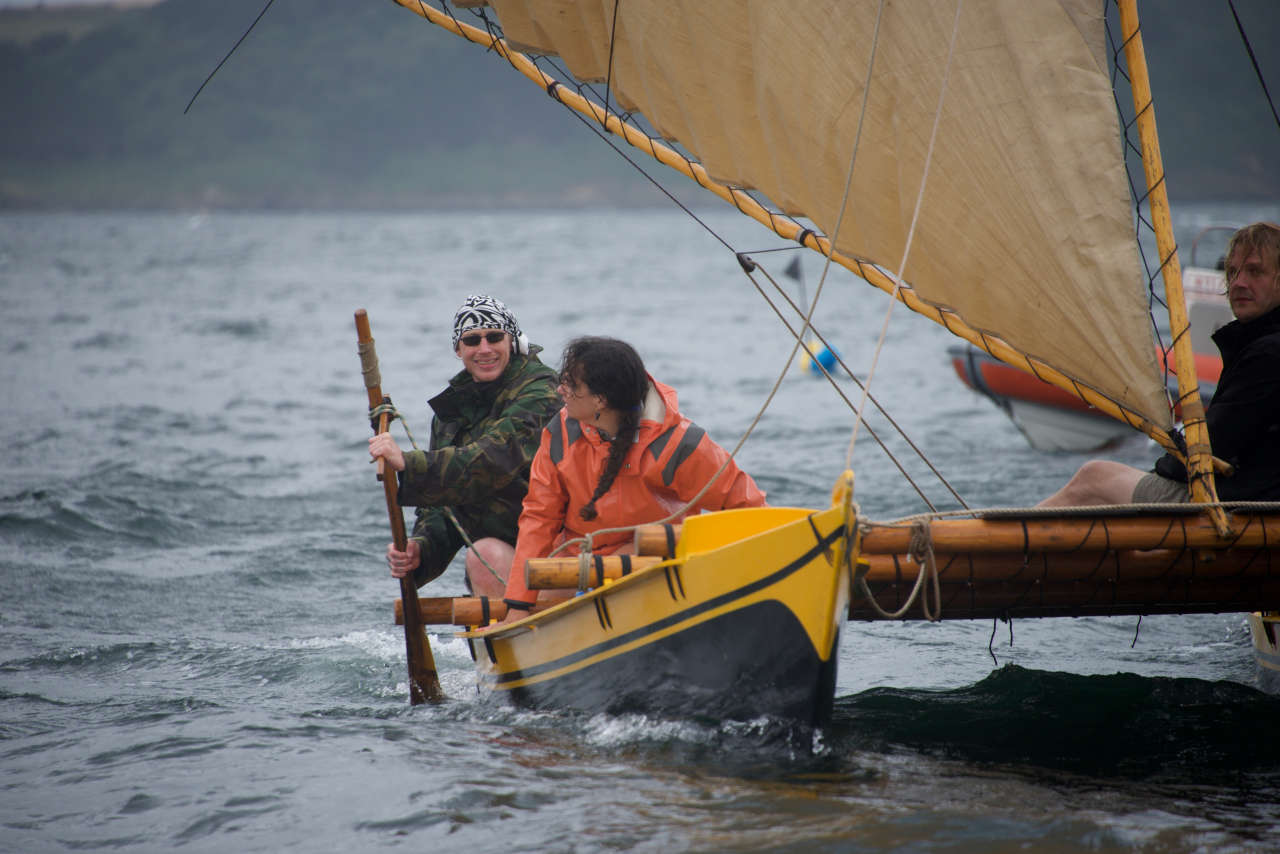 Three people on a black and yellow ethnic double canoe