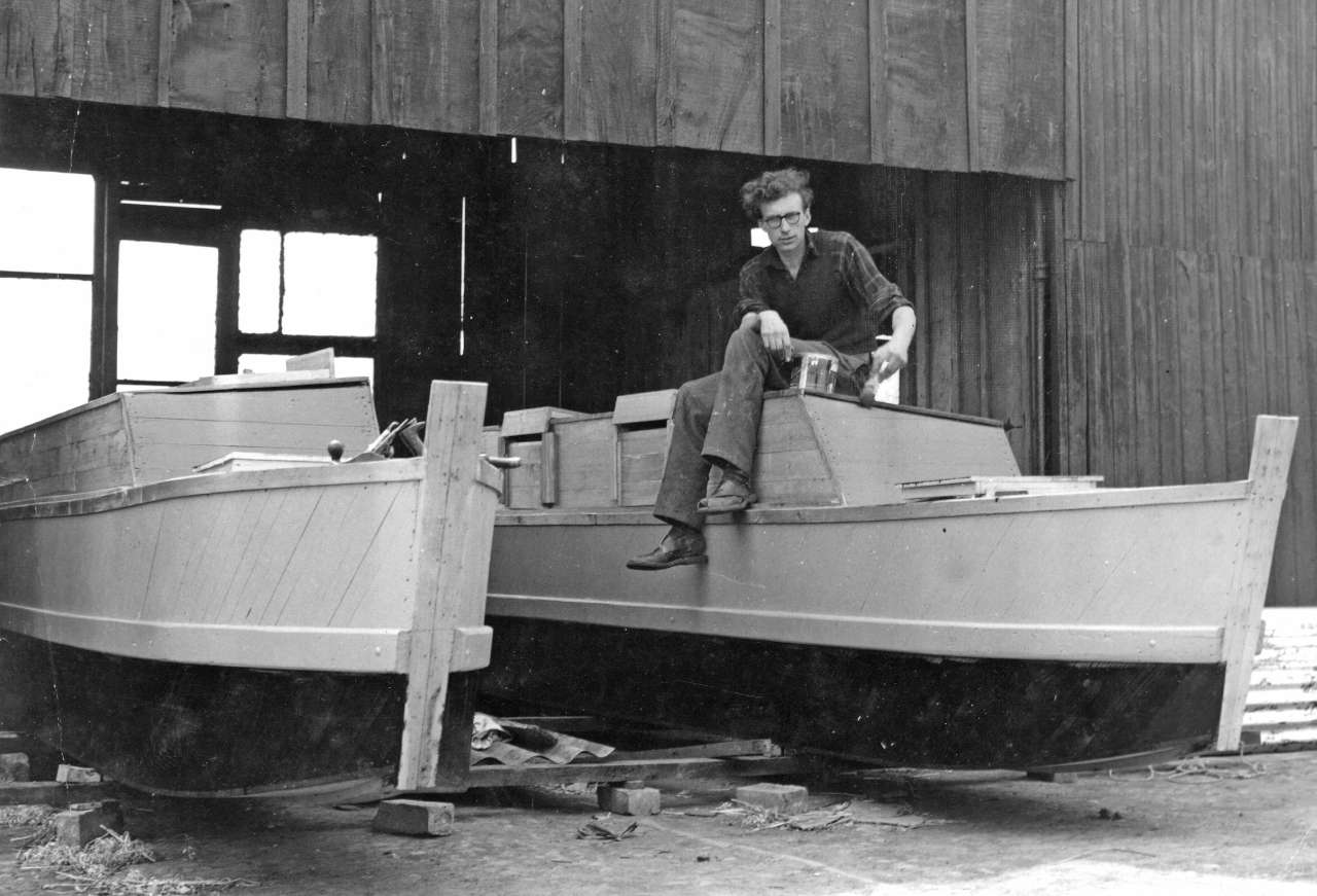 A man sitting on the hull of a double canoe under construction