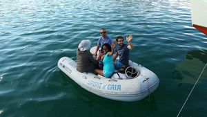 Four crew members in rubber dinghy, waving